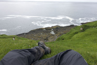 Low section of man sitting on hill against sea