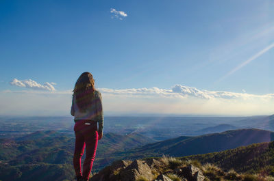 Rear view of woman standing on mountain against sky