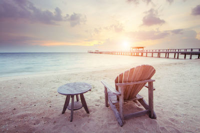 Chairs and table on beach against sky during sunset