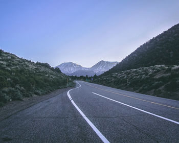 Road leading towards mountains against clear sky