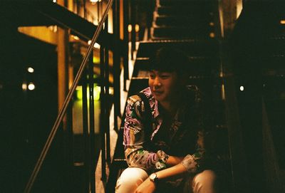 Young man looking away while sitting in illuminated room