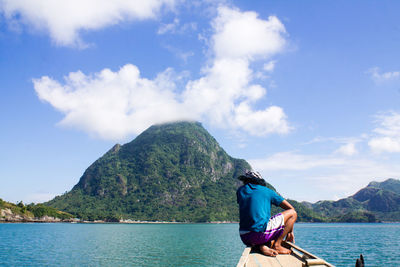 Rear view of man sitting on boat over sea against sky