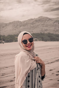 Portrait of young woman wearing sunglasses standing on beach