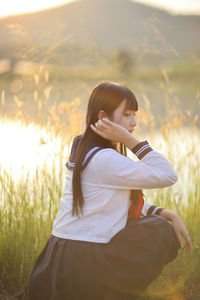 Side view of young woman sitting on field