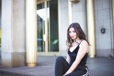 Portrait of young woman sitting on footpath in city