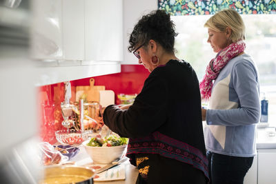 Multi-ethnic friends preparing salad in kitchen at home