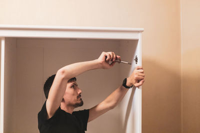 A young man is tightening the screws on the fittings inside the wardrobe.