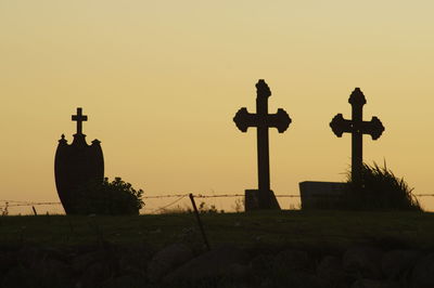 Silhouette cross in cemetery against sky during sunset