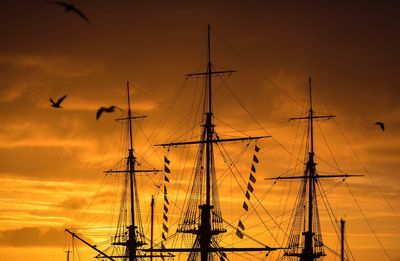 Low angle view of silhouette sailboats against orange sky