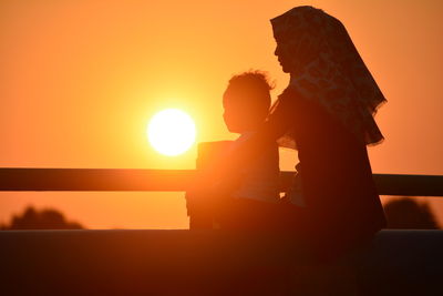 Silhouette people sitting against orange sky during sunset