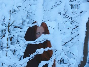 Portrait of young woman through snow covered tree