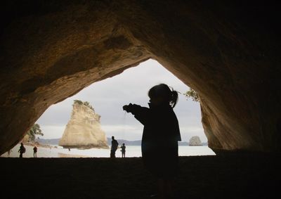 Side view of silhouette girl standing under cave at beach