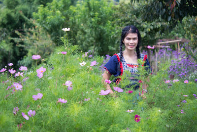 Smiling woman with pink flowers against plants