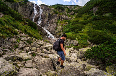 Man hiker tourist with backpack walks on a rocky mountain terrain a huge waterfall in the mountains