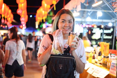 Portrait of smiling mid adult woman holding ice cream in city at night