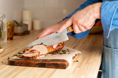 Unrecognizable man cuting with large knife baked pork tenderloin on cutting board 