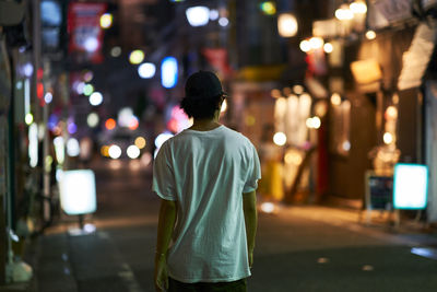 Rear view of man walking on illuminated city at night
