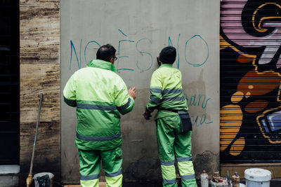 Rear view of men making graffiti on concrete wall