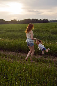 Mom and daughter in white t-shirts and denim shorts have fun on a green field in summer