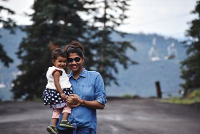 Portrait of smiling woman holding daughter while standing on road