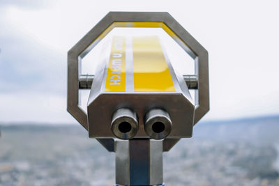 Close-up of yellow coin-operated binoculars against sky