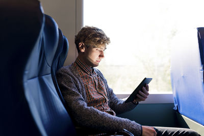 Young man sitting in a train looking at tablet