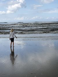 Rear view of girl standing at beach against sky