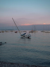 Sailboats moored in sea against sky during sunset