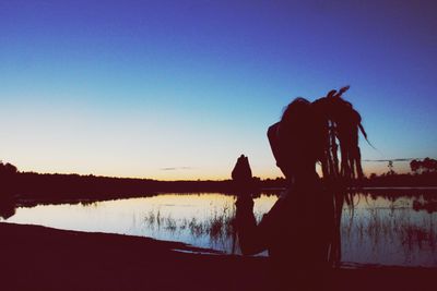 Silhouette people standing by lake against sky during sunset
