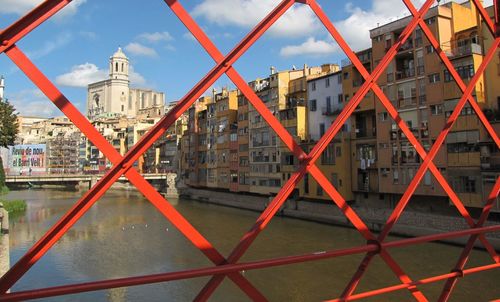 Onyar river by buildings and girona cathedral seen through orange metal grid