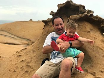 Cheerful father and son sitting at beach