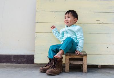 Full length of boy sitting against wall