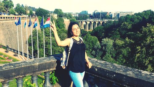 Portrait of smiling woman showing peace sign while standing on building terrace