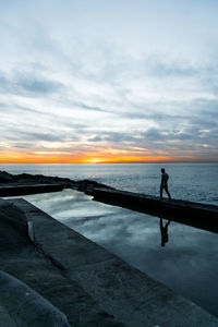 Silhouette man standing on sea against sky during sunset