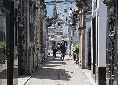 Rear view of people walking on footpath amidst buildings in city