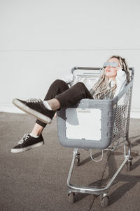 Young woman with dreadlocks sitting in shopping cart against wall