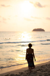 Rear view of woman walking on beach during sunset