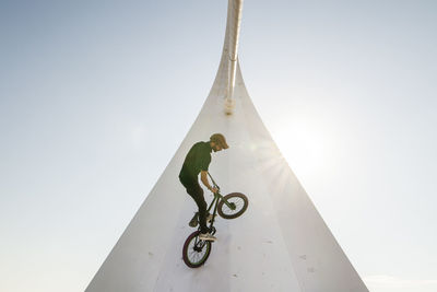 Man riding bicycle on built structure against sky