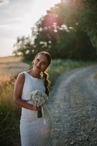 Portrait of smiling bride with bouquet standing on country road