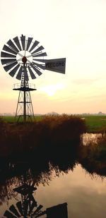 Traditional windmill by lake against sky during sunset