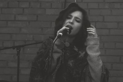 Young woman singing against brick wall