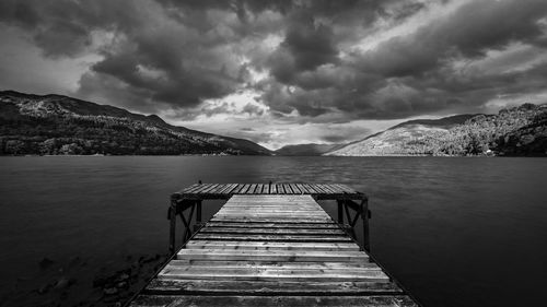 Pier over lake against cloudy sky