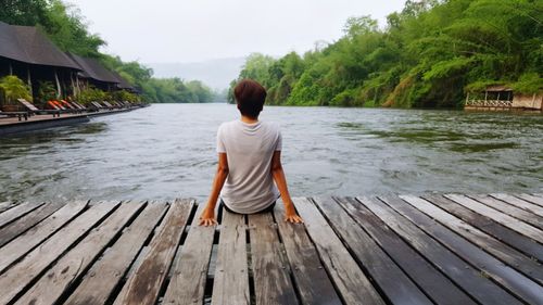 Rear view of mature man sitting on bridge over river