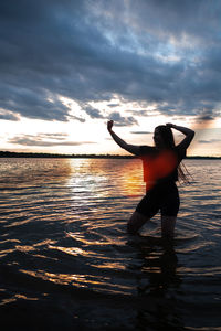 Rear view of woman standing at beach during sunset