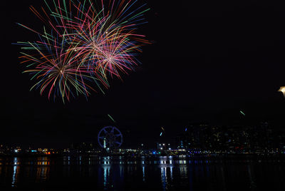 Firework display over illuminated city against sky at night