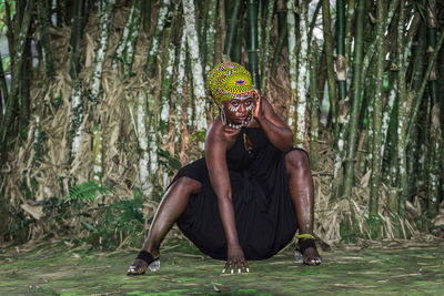African woman sitting in front of bamboo forest with african face painting.