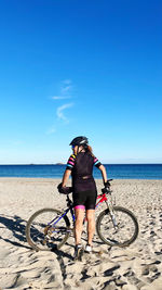 Rear view of man riding bicycle on beach against clear blue sky