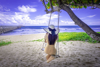 Rear view of woman sitting on swing on beach