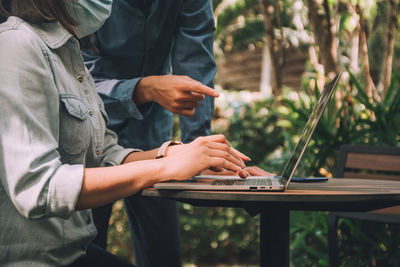 Midsection of businesswoman using laptop with colleague outdoors