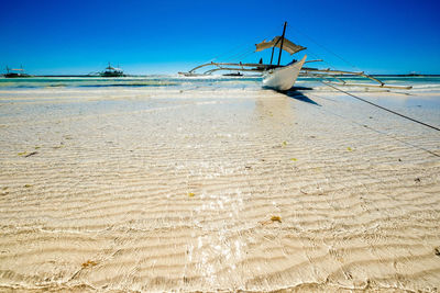 Outrigger boat moored at beach against sky